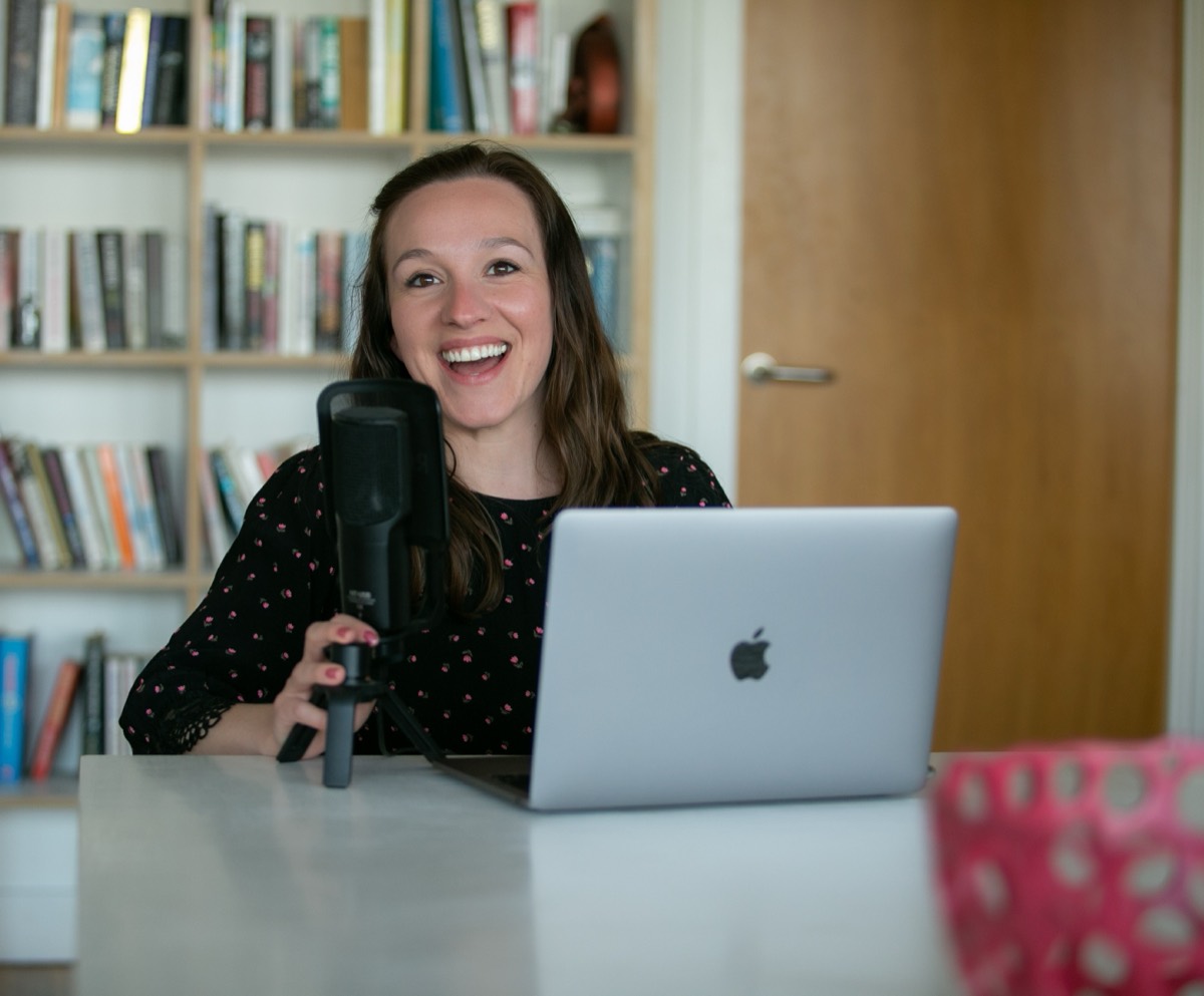 Cordelia Kate laughing at her desk behind a microphone and a laptop